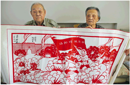 薛贵生和爱人王继兰展示剪纸纪念品《沾阳棣独立团》